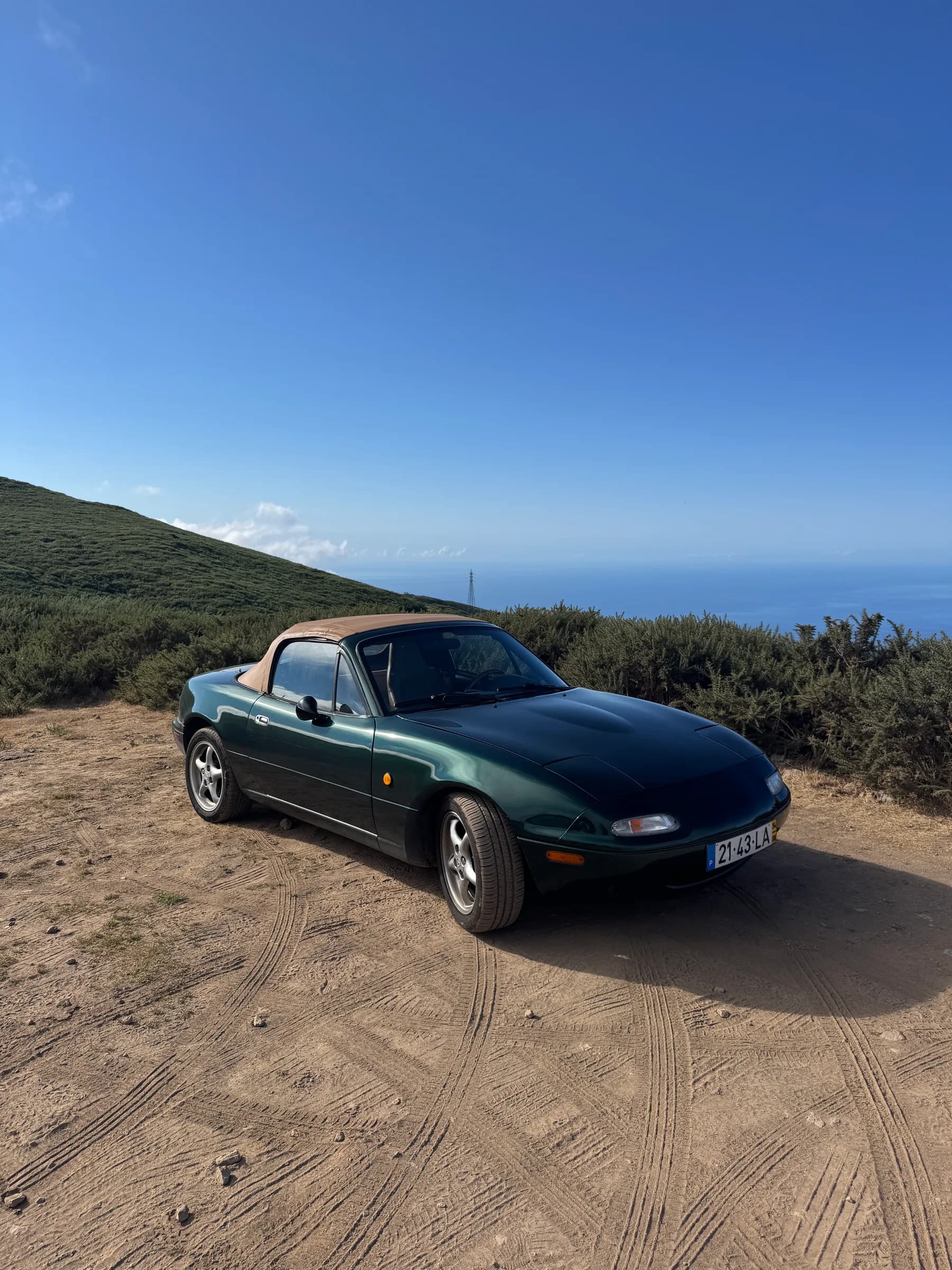 MX-5 com o soft-top bege levantado, de três quartos, com o céu limpo ao fundo