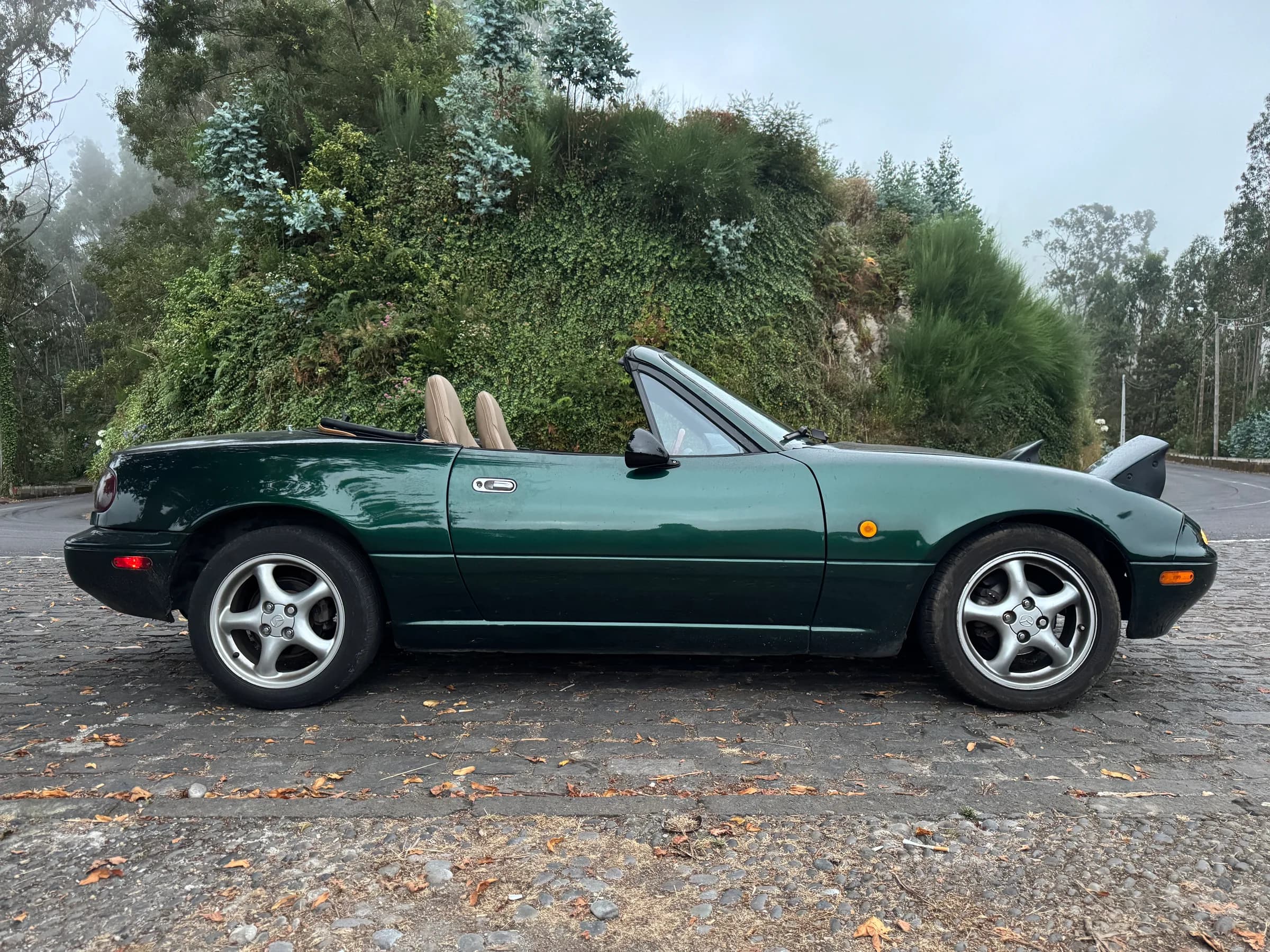 Mazda MX-5 de 1994, verde escuro, visto de perfil com a capota baixada
